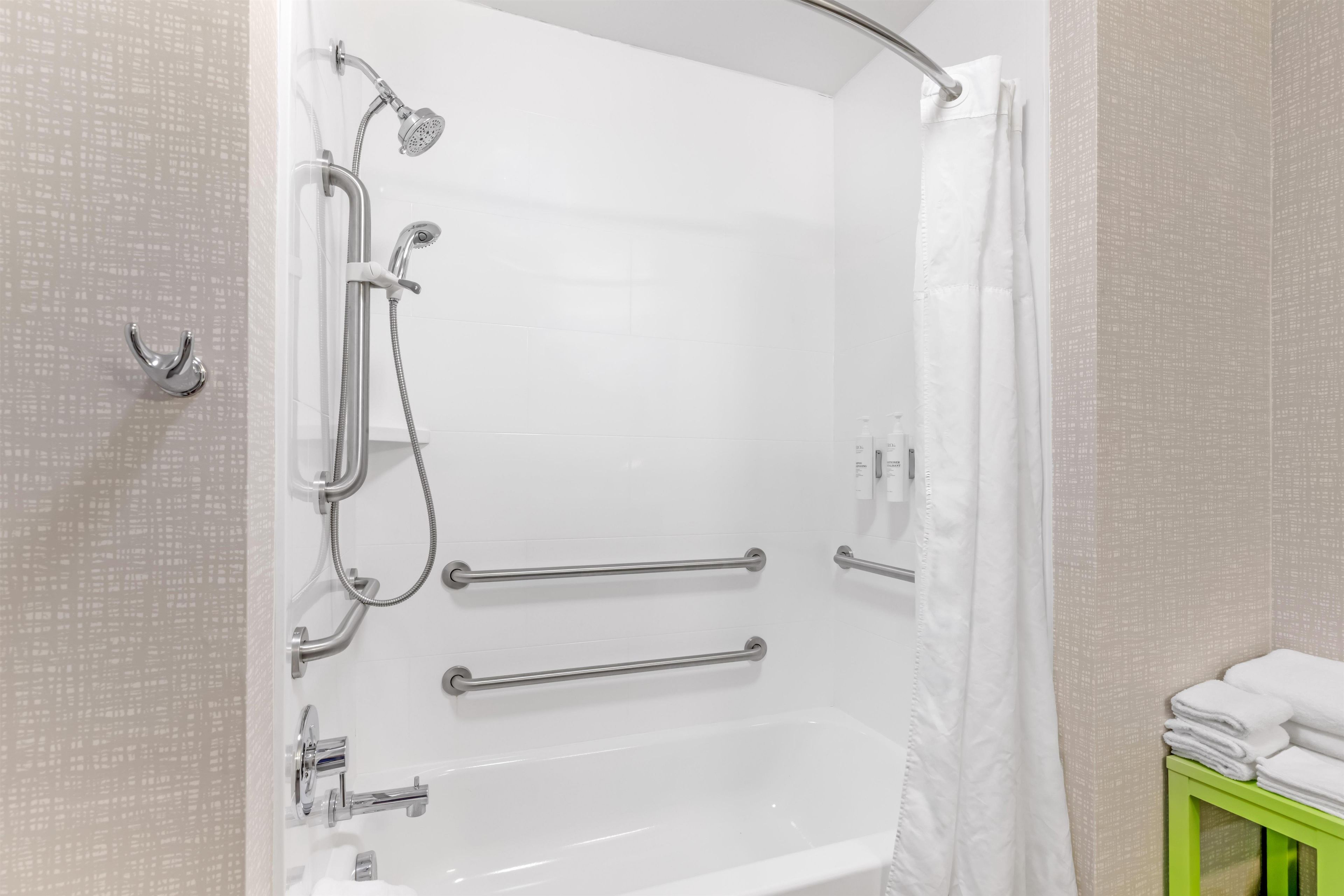 A shower with a handheld showerhead, grab bars, and a non-slip floor.