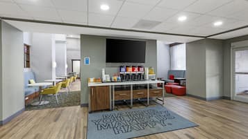 A modern indoor space with a coffee station, seating area, and a large flat-screen TV mounted on the wall.