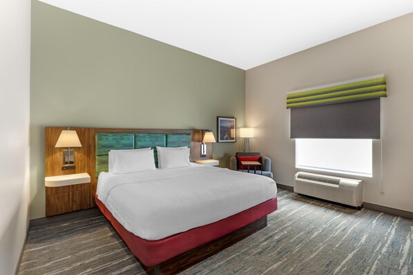 A hotel room with a bed, two bedside lamps, a nightstand, a window with blinds, and a wall-mounted air conditioner.
