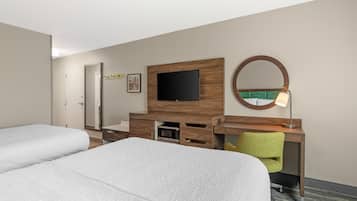 Een hotelkamer met twee bedden, een bureau met een televisie, een spiegel en een lamp.