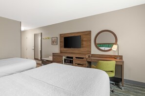 Habitación de hotel con dos camas, un escritorio con televisor, un espejo y una lámpara.