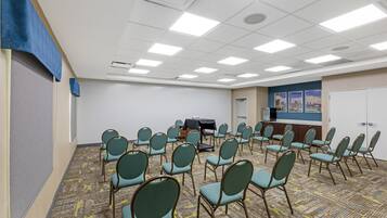 Un salón de conferencias con filas de sillas, un proyector y una pantalla para presentaciones.