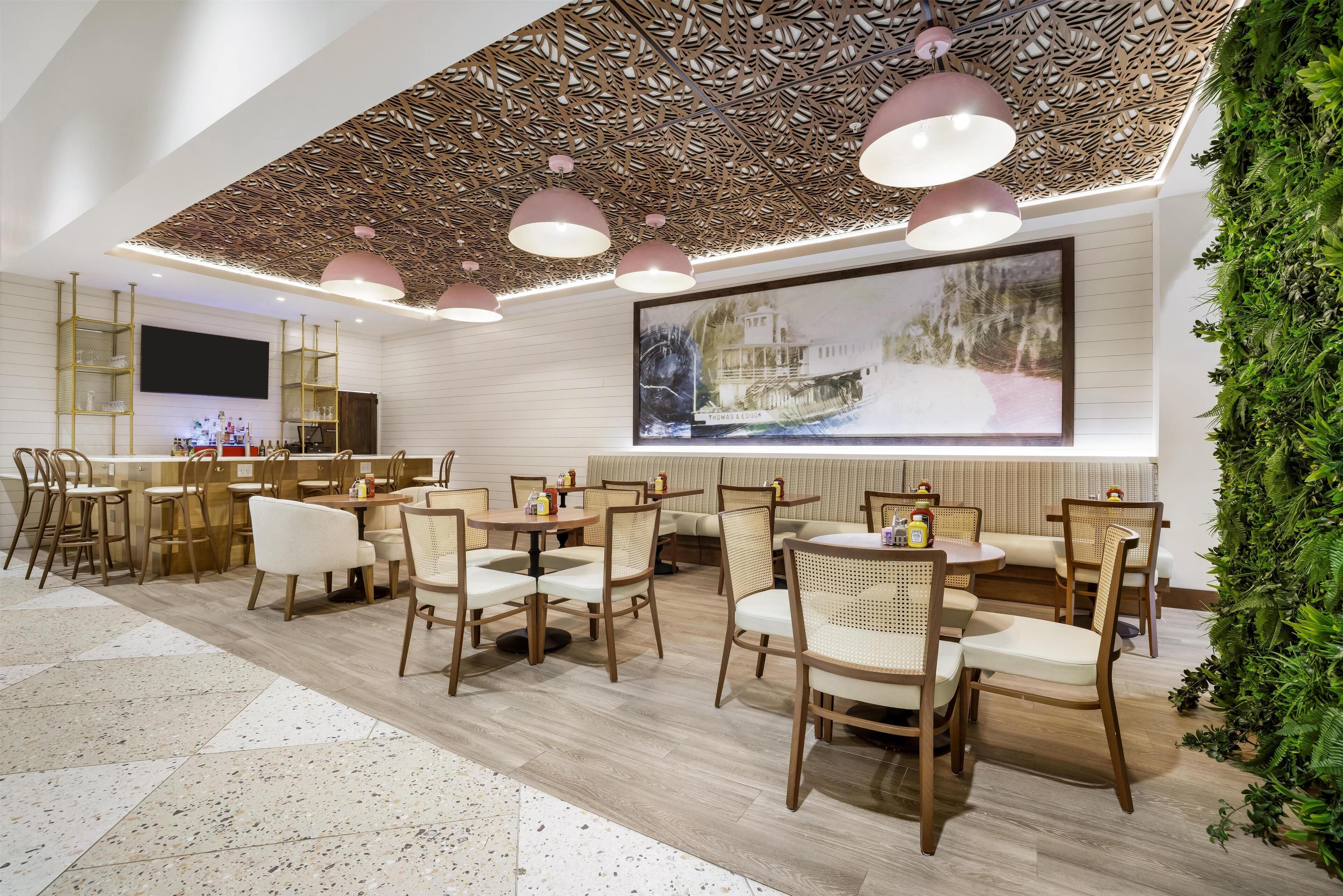 Un interior de restaurante moderno con muebles de madera, un cuadro grande en la pared y una pared verde con plantas.