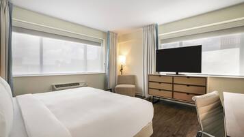 Habitación de hotel con una cama grande, un escritorio, una silla, un televisor y una ventana con cortinas.