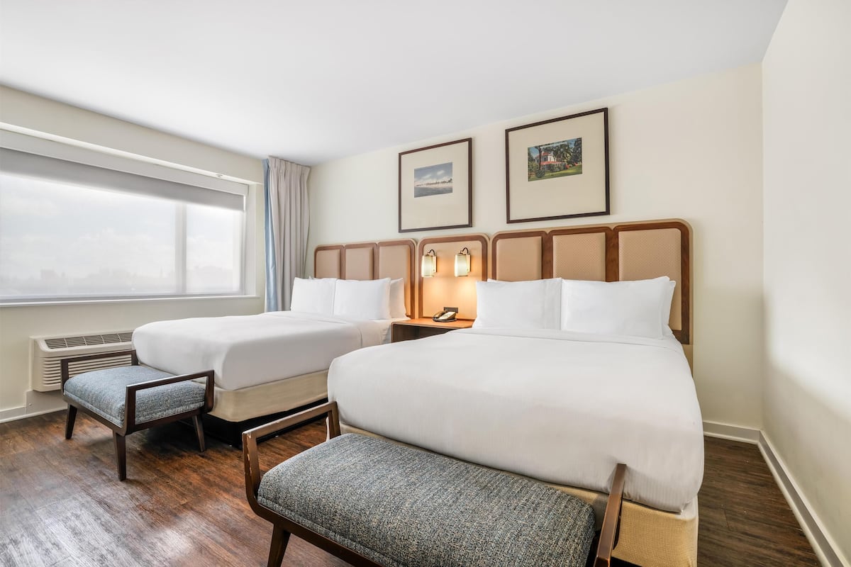 Ein Hotelzimmer mit zwei Betten, einem Vorhangfenster, einem Heizkörper und zwei gerahmten Bildern an der Wand.
