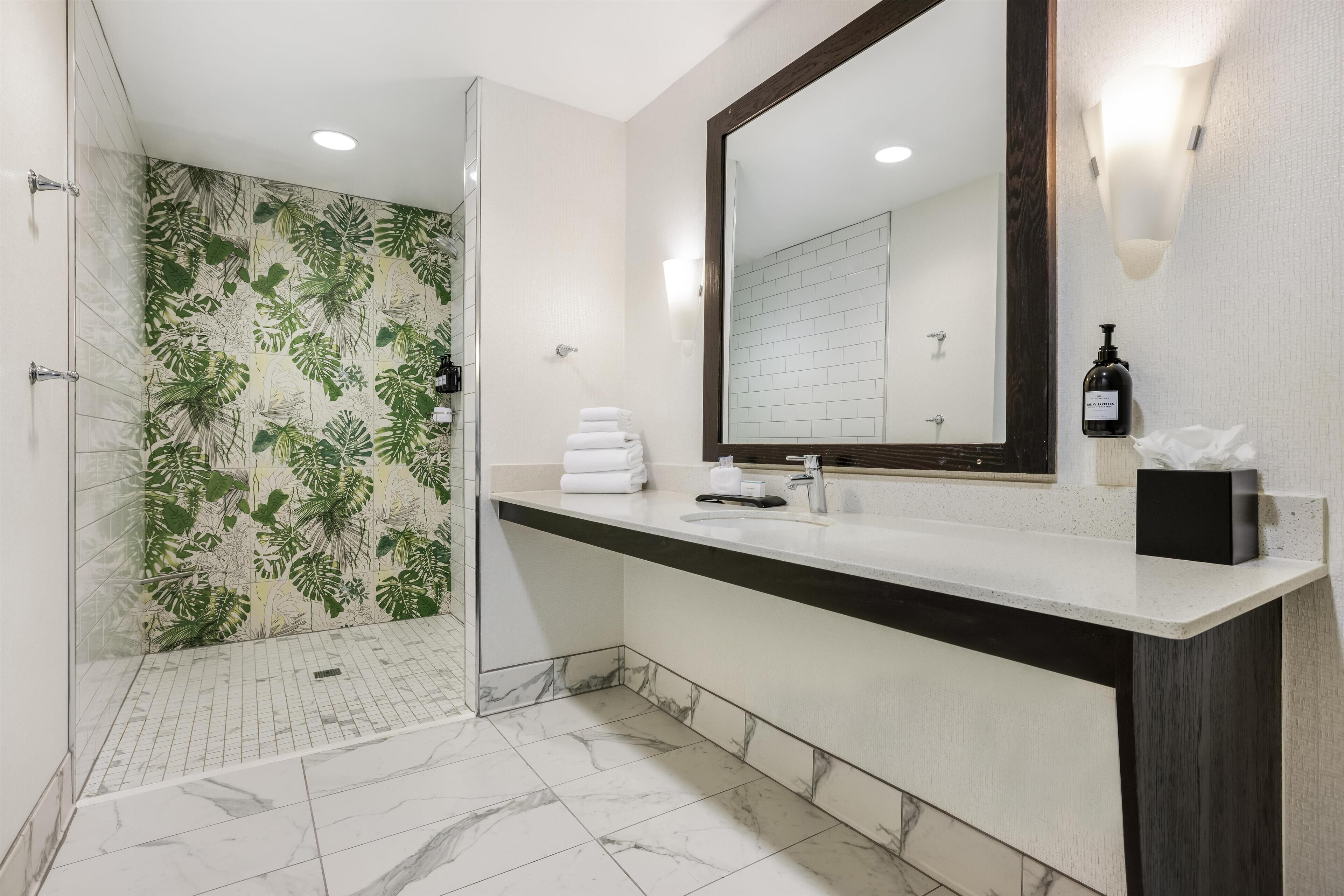A modern bathroom with a shower, a large mirror, and a vanity with a bottle of lotion.