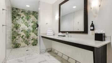 Une salle de bain moderne avec une douche, un grand miroir et un meuble-lavabo agrémenté d’un flacon de lotion.