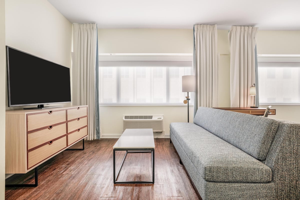 Ein modernes Wohnzimmer mit Flachbildfernseher, Holzschrank, grauem Sofa und weißem Couchtisch.