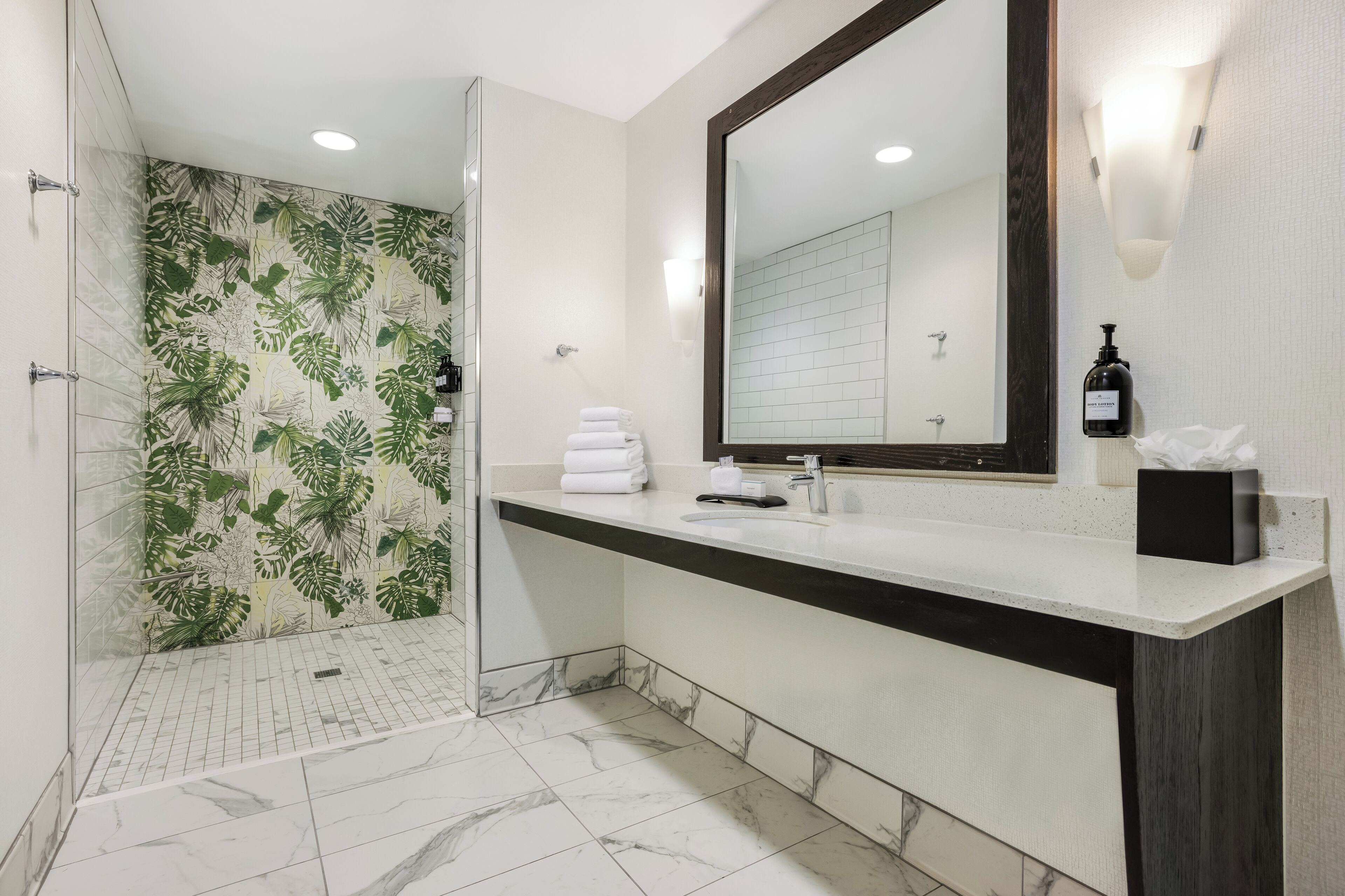 A modern bathroom with a shower, a large mirror, and a vanity with a marble countertop.