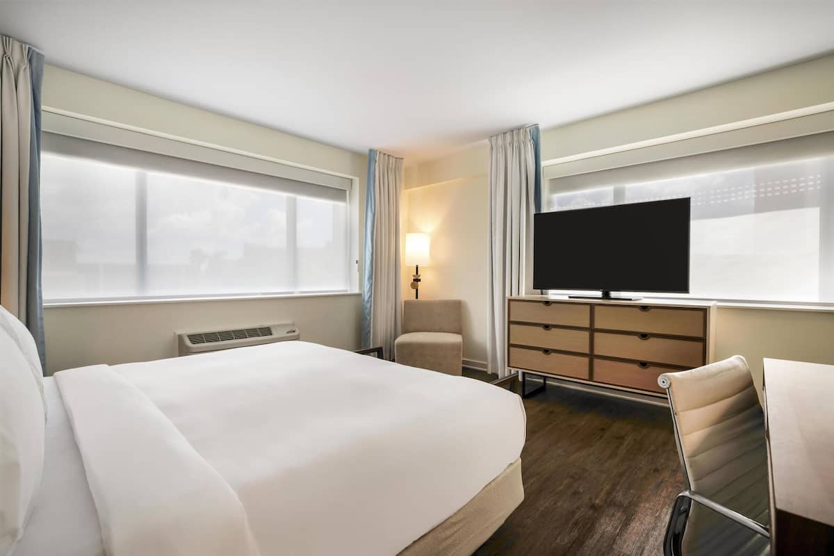 Ein Hotelzimmer mit einem großen Bett, einem Fernseher, einem Schreibtisch und einem Sessel.