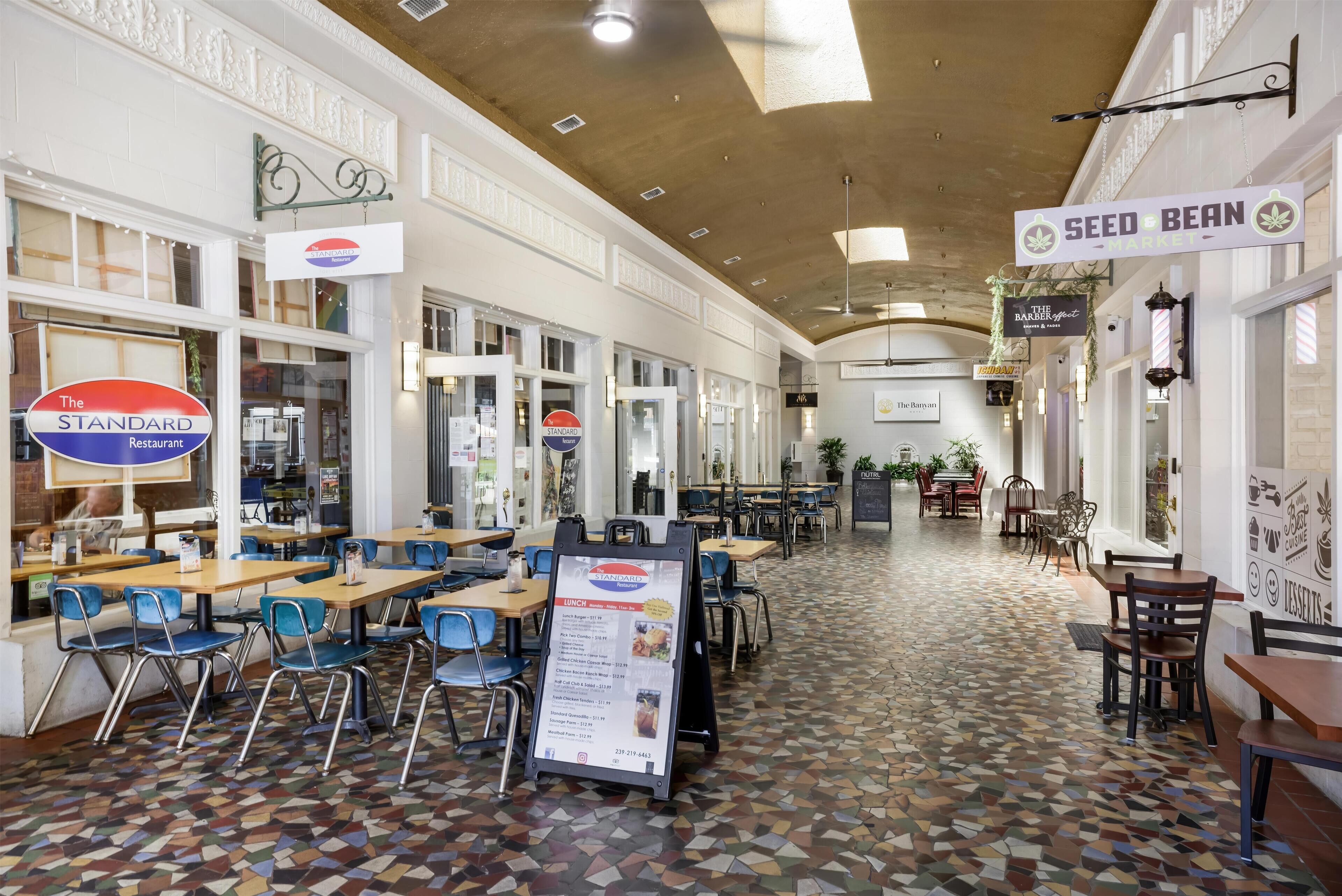 A spacious indoor area with multiple dining tables and chairs, a patterned floor, and various signs for different businesses.