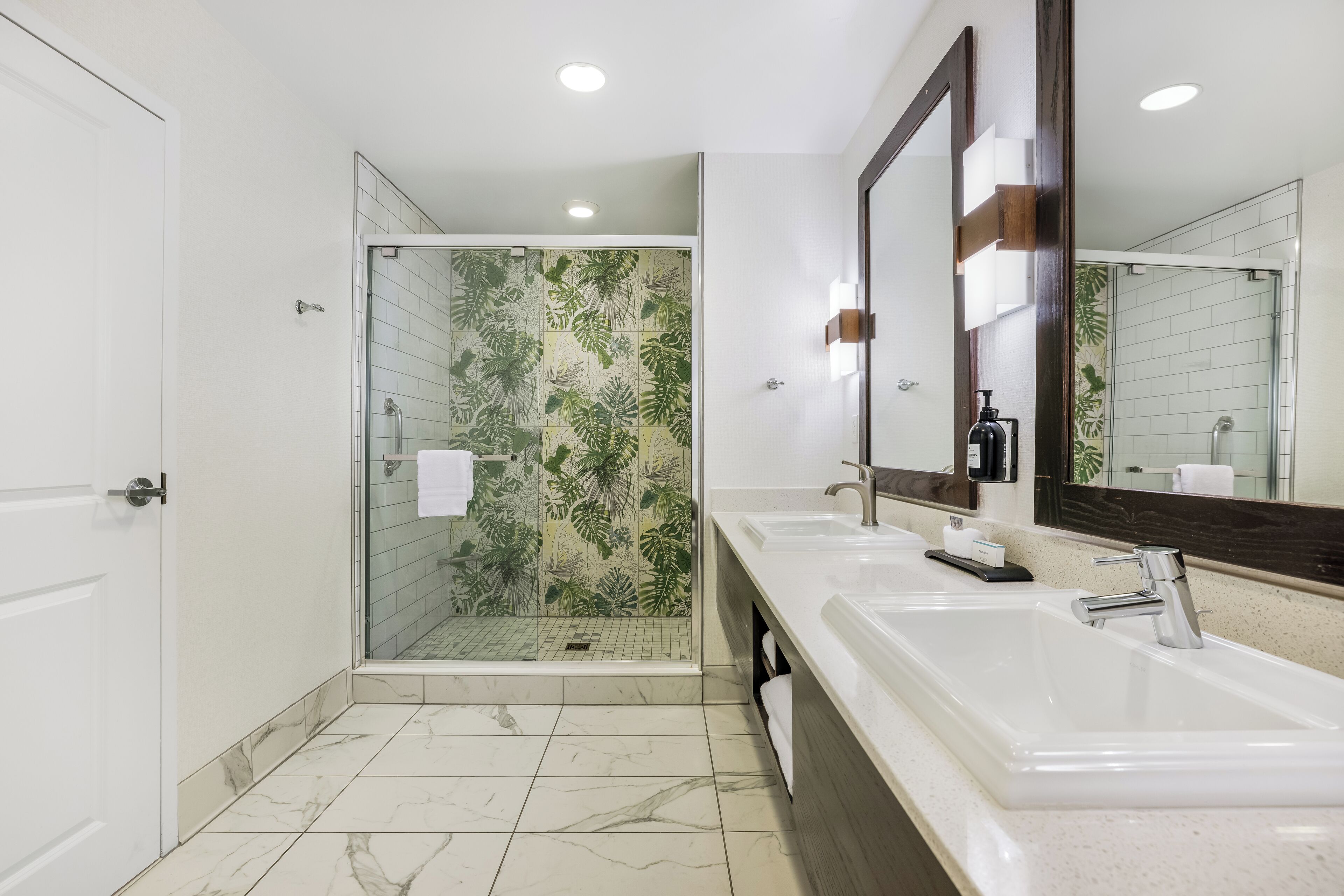 Une salle de bain moderne avec une douche à l’italienne en verre, deux vasques et un grand miroir.