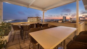 Een terras op het dak met een tafel en stoelen, met uitzicht op een stadsbeeld in de schemering.