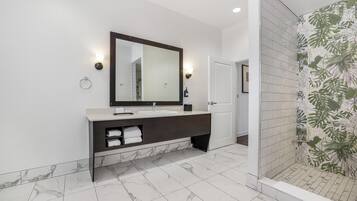 Un baño moderno con lavamanos de mármol, un espejo grande y una ducha con un diseño de plantas en la pared.