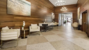 Een moderne hotel lobby met houten lambrisering, een groot abstract schilderij, een kroonluchter, een zithoek met een ronde tafel en een bar.