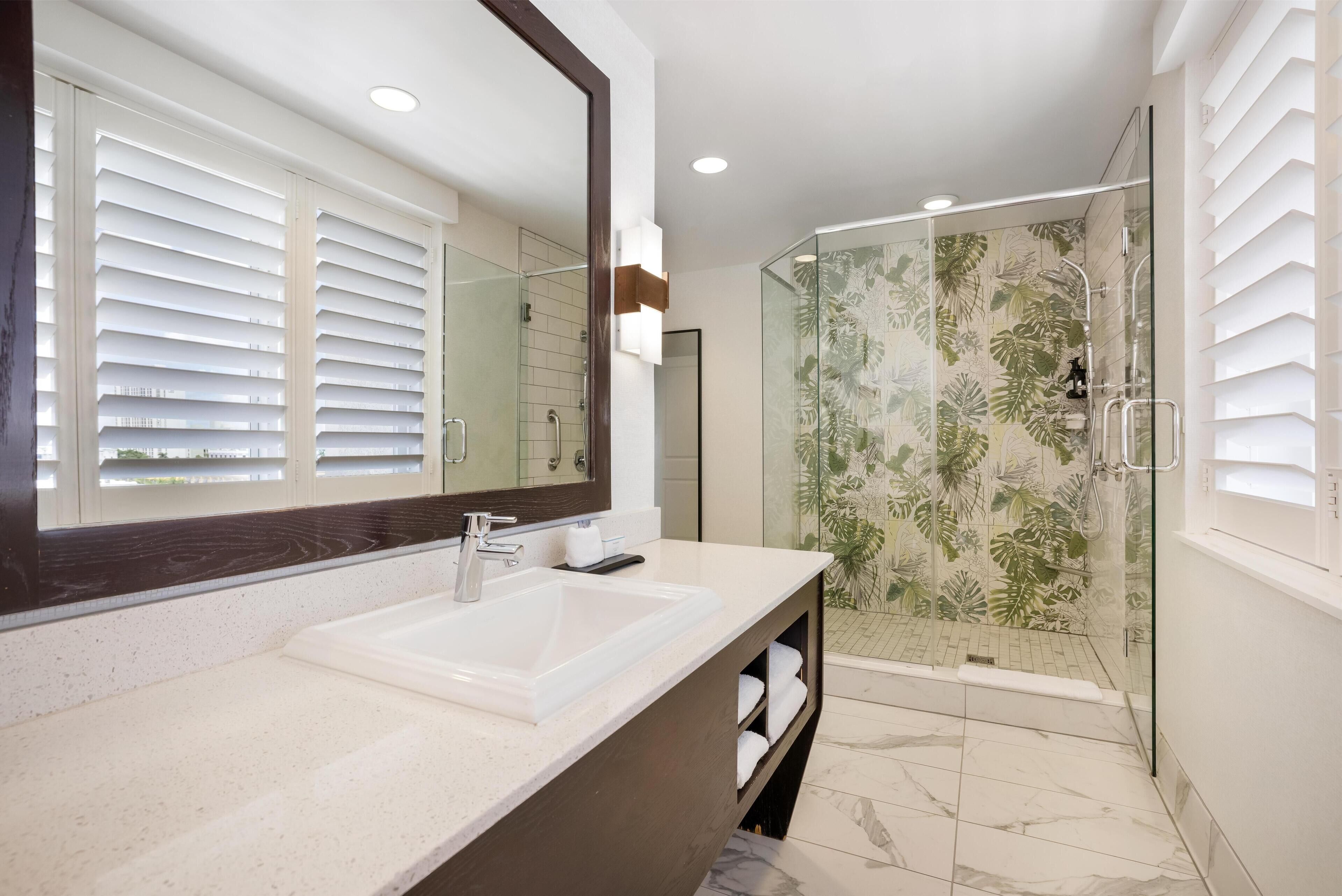 A bathroom with a large mirror, a sink, and a shower with glass doors.