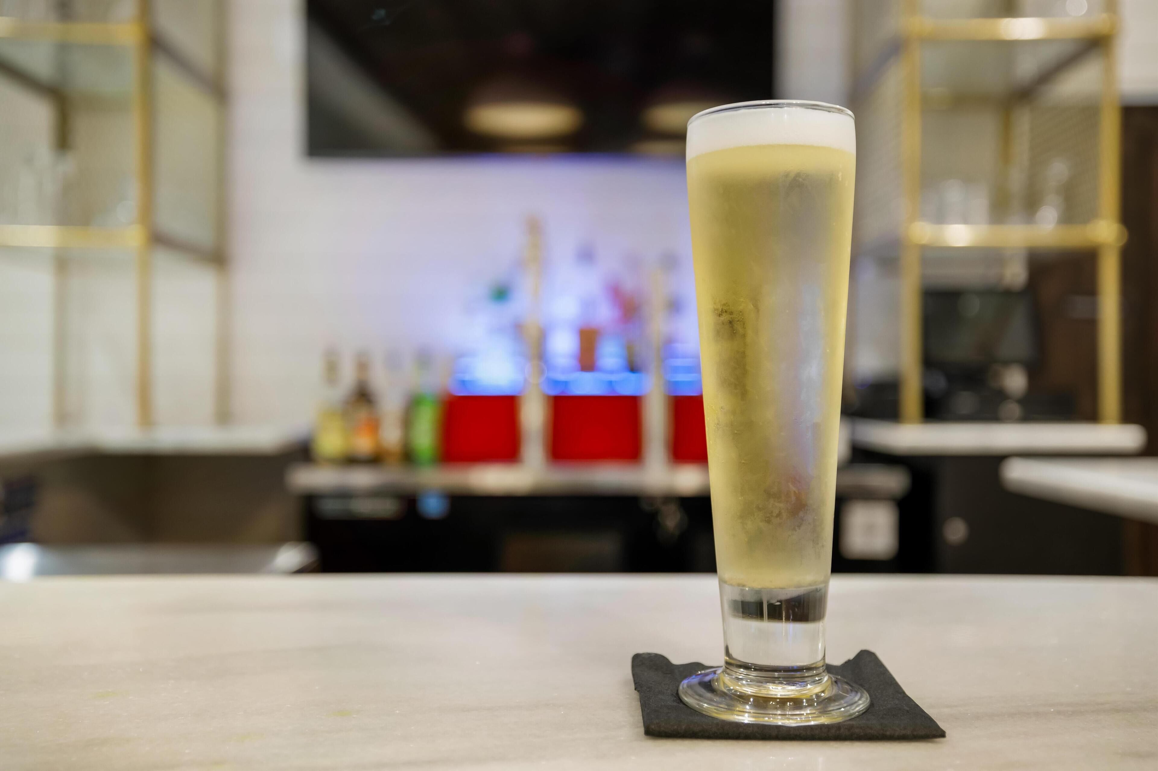 A tall glass of beer on a coaster in a bar setting.