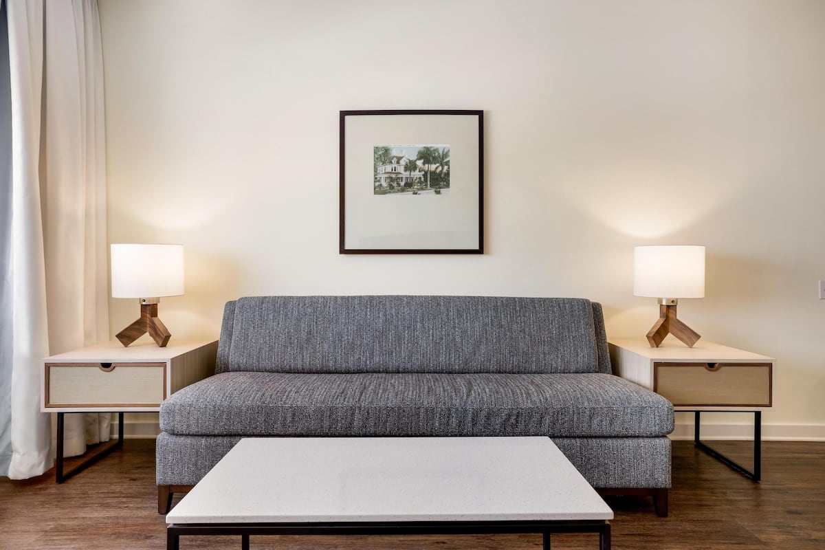 Ein modernes Wohnzimmer mit einem grauen Sofa, zwei Nachttischen mit Lampen, einem gerahmten Bild an der Wand und einem weißen Couchtisch.