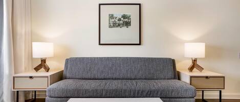 A modern living room with a grey sofa, two bedside tables with lamps, a framed picture on the wall, and a white coffee table.