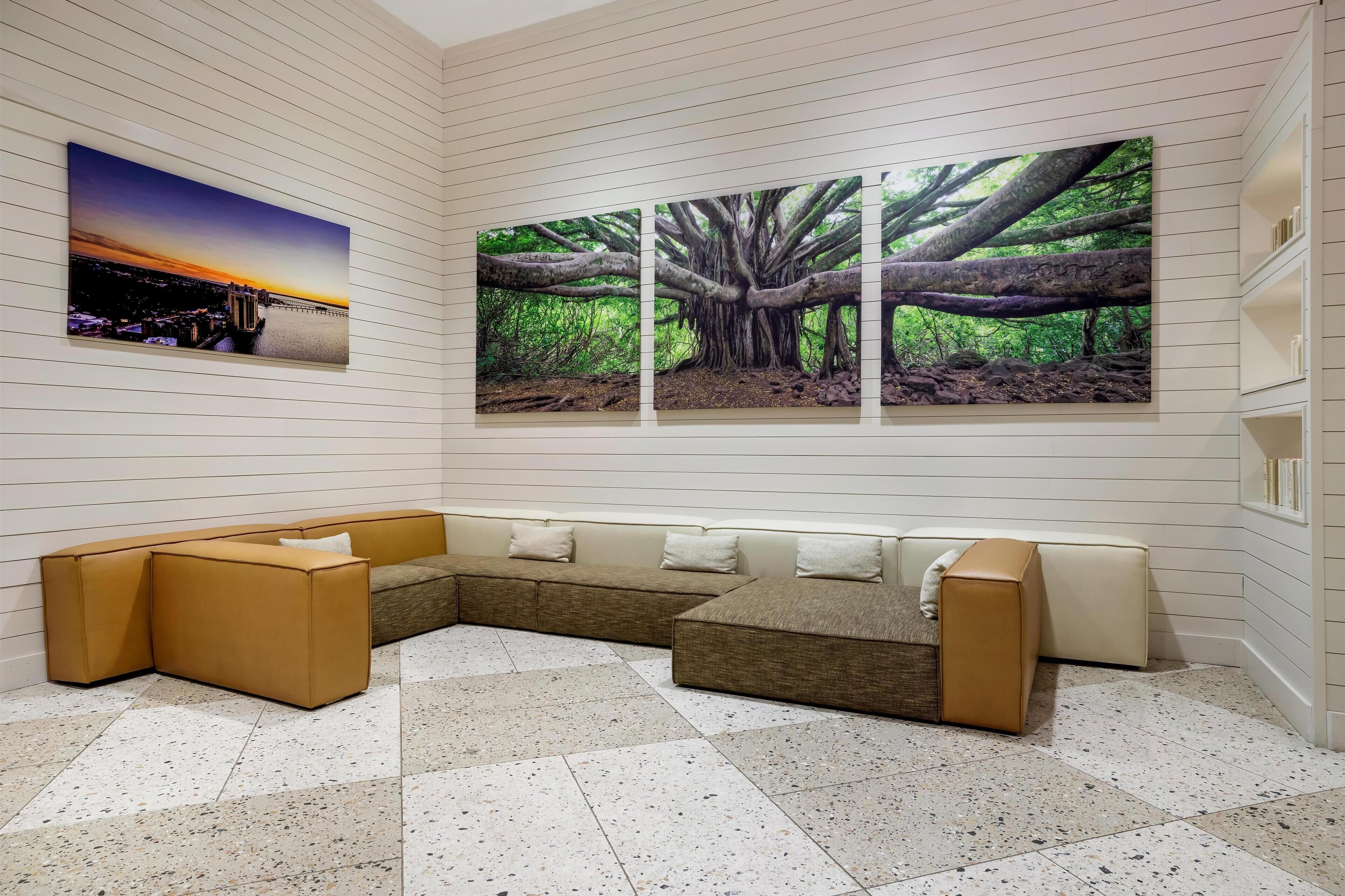 Zona d'estar moderna amb un sofà modular, una obra d'art penjada a la paret que representa un capvespre i un arbre, i un sòl de rajola.