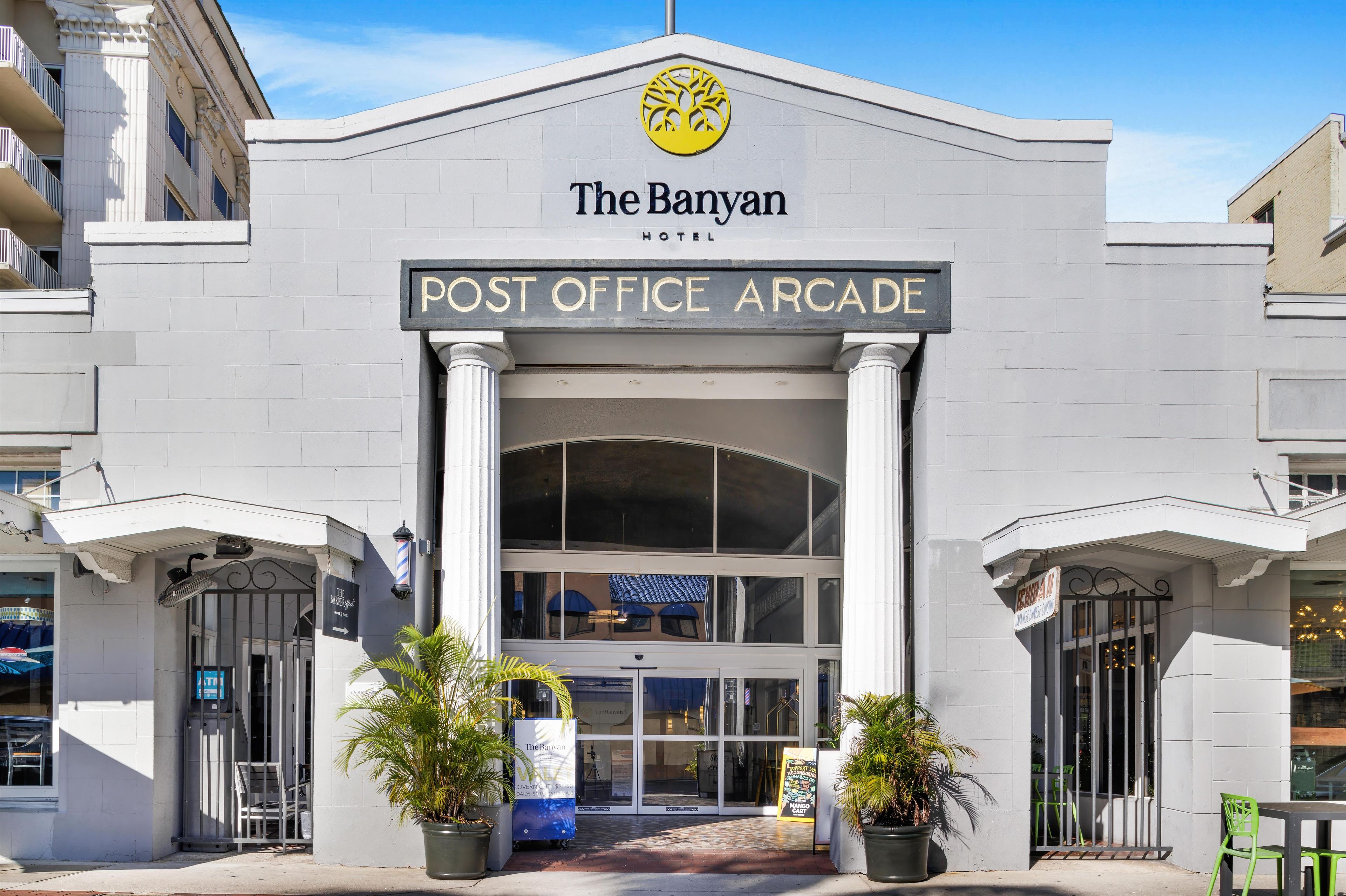 The Banyan Hotel's Post Office Arcade entrance with a double door, potted plants, and a clear sky.