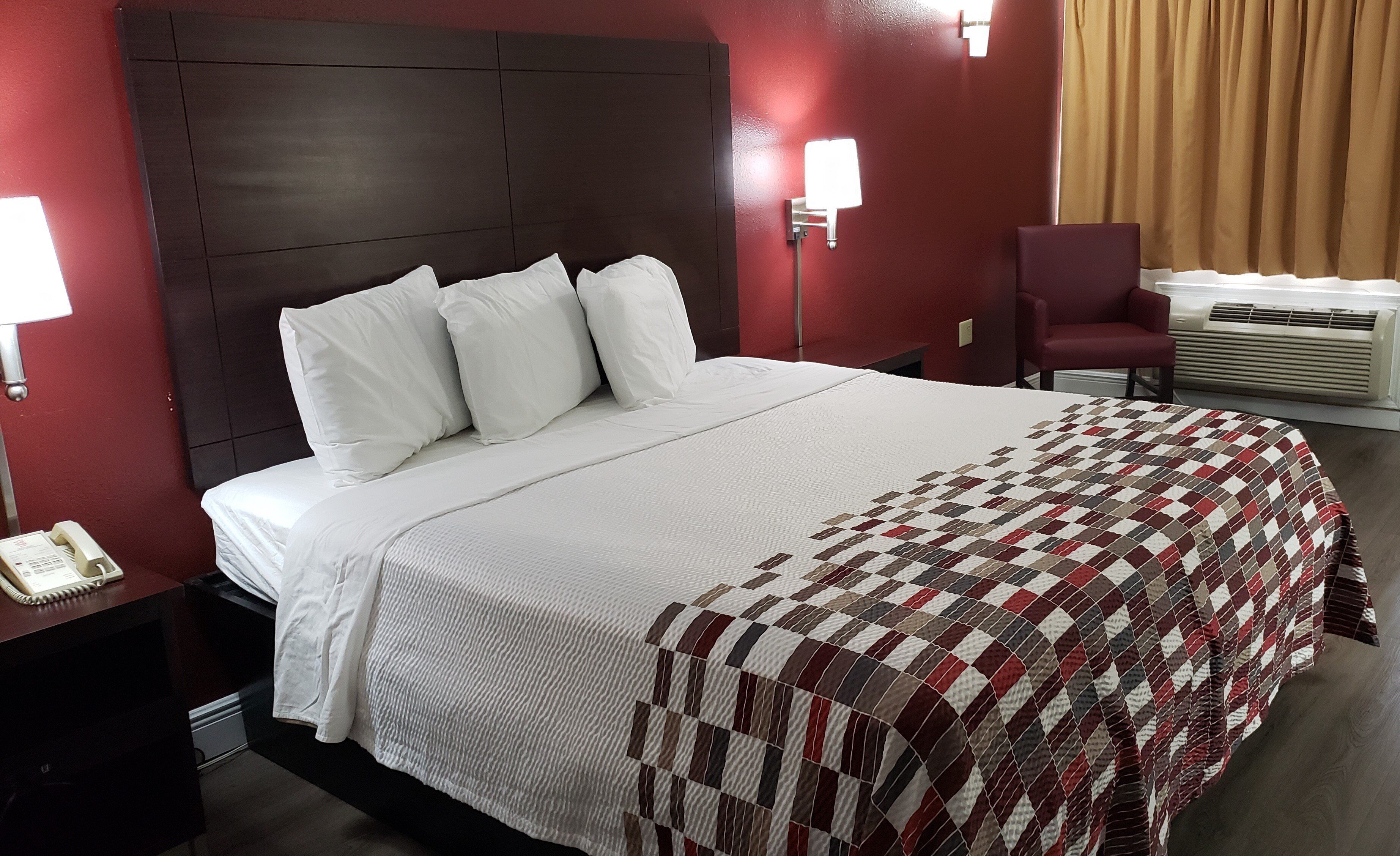 Une chambre d’hôtel avec un grand lit, un bureau avec un téléphone, une chaise et une fenêtre avec des rideaux.