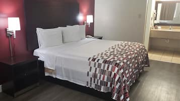 A hotel room with a bed, bedside tables, a nightstand, a wall-mounted lamp, a telephone, and a bathroom visible through an open door.