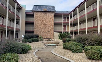 A multi-story hotel with a central stone pillar, balconies, and a gravel pathway.