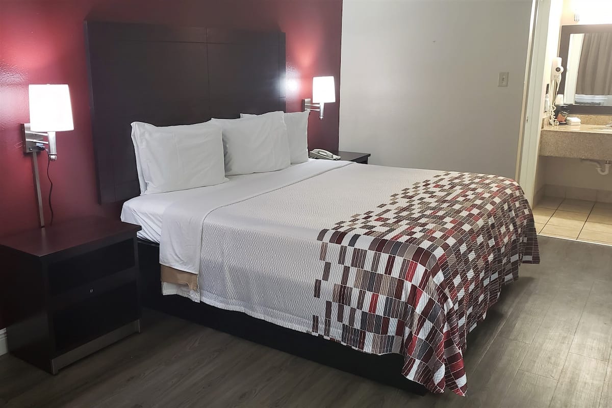 Ein Hotelzimmer mit Bett, Nachttisch, Nachttischlampe, Telefon und einem durchgegangenen Tür erkennbaren Badezimmer.