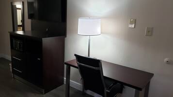 A hotel room with a desk, chair, lamp, and a dark-colored dresser.