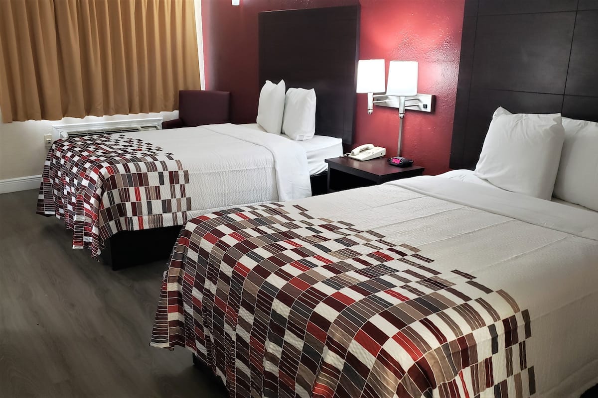 Ein Hotelzimmer mit zwei Betten, jeweils mit karierter Bettdecke, einem Nachttisch mit Lampe und einem Telefon.