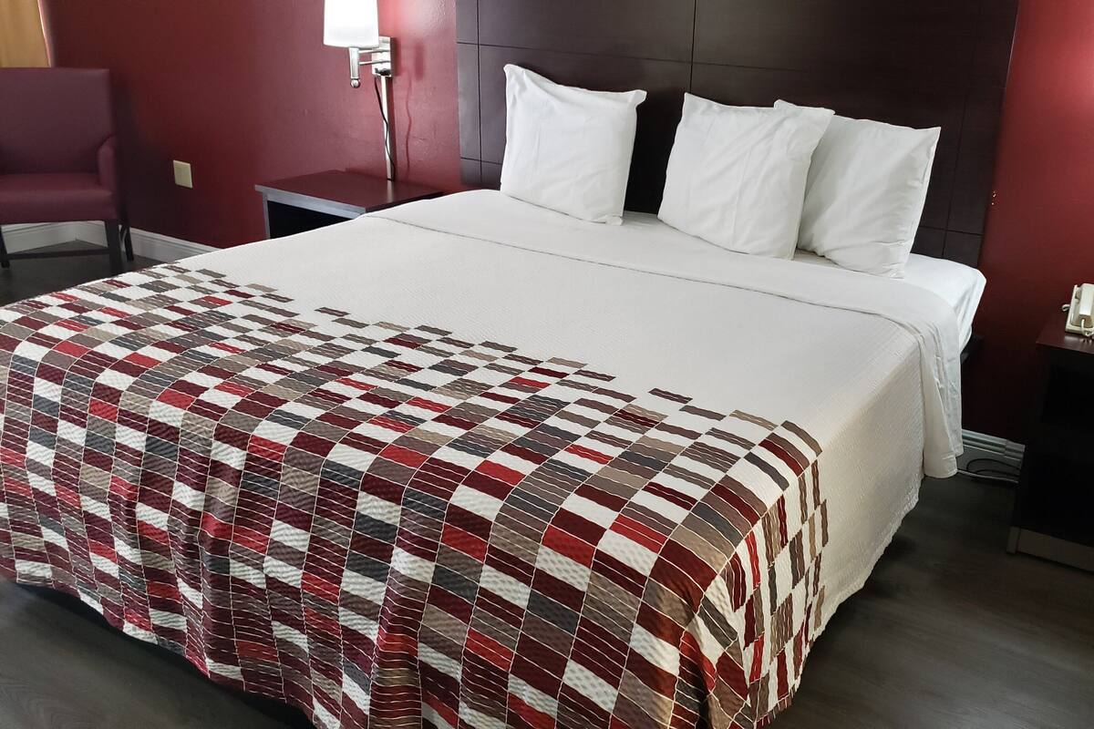 Ein ordentlich bezogenes Bett mit kariertem Überwurf, weißen Kissen und einem dunklen Kopfteil.