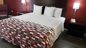 A neatly made bed with a checkered bedspread, white pillows, and a dark headboard. - Red Roof Inn Kenner – New Orleans Airport NE (Kenner)
