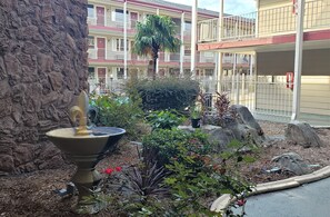 A courtyard with a fountain, various plants, and a stone wall. - Red Roof Inn Kenner – New Orleans Airport NE (Kenner)