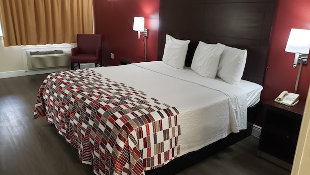 Hotellihuone, jossa on suuri sänky, punainen nojatuoli, kirjoituspöytä puhelimineen ja seinään kiinnitetty lamppu.