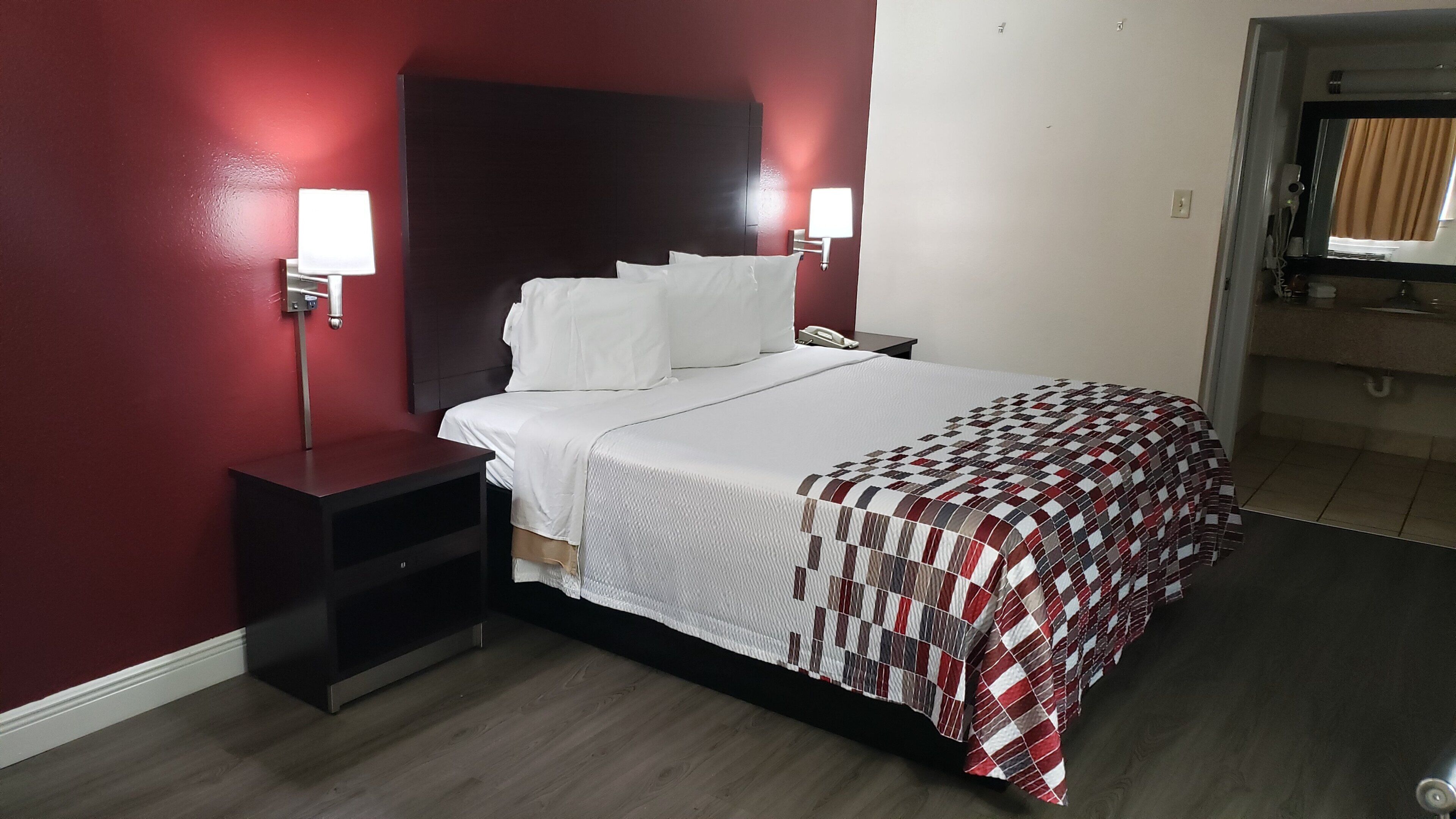 Une chambre d’hôtel avec un lit, des tables de chevet, un mur rouge et une fenêtre.