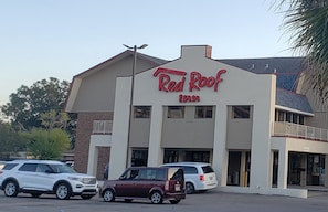A Red Roof Inn building with a flat roof and a large sign. There are three vehicles parked in front.