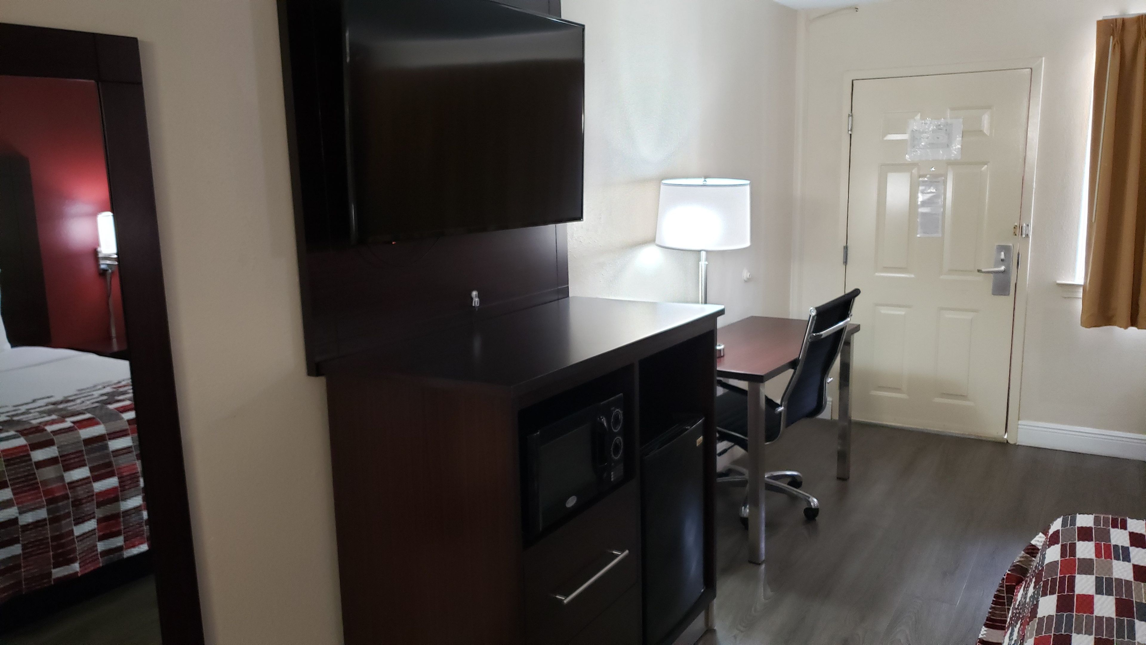 A hotel room with a bed, a desk with a chair, a television, and a door.