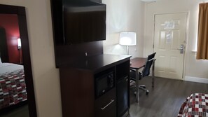 A hotel room with a bed, a desk with a chair, a television, and a door. - Red Roof Inn Kenner – New Orleans Airport NE (Kenner)