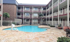 A courtyard with a swimming pool, stone flooring, and a multi-story building with balconies. - Red Roof Inn Kenner – New Orleans Airport NE (Kenner)