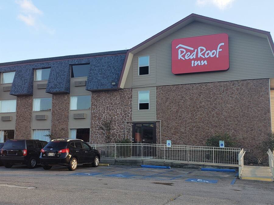 Edificio RedRoof Inn con fachada de piedra, múltiples ventanas y estacionamiento con coches.