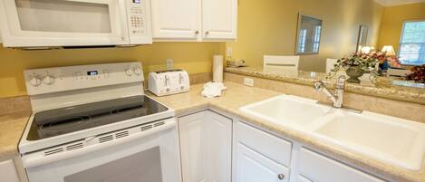 A kitchen with white cabinets, a microwave, a stove, a toaster, and a sink.