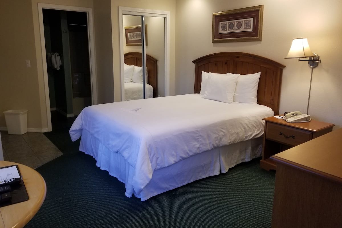 A hotel room with a large bed, a bedside lamp, a telephone, and a desk with a laptop.