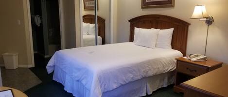 Una habitación de hotel con una cama grande, una lámpara de noche, un teléfono y un escritorio con una computadora portátil.