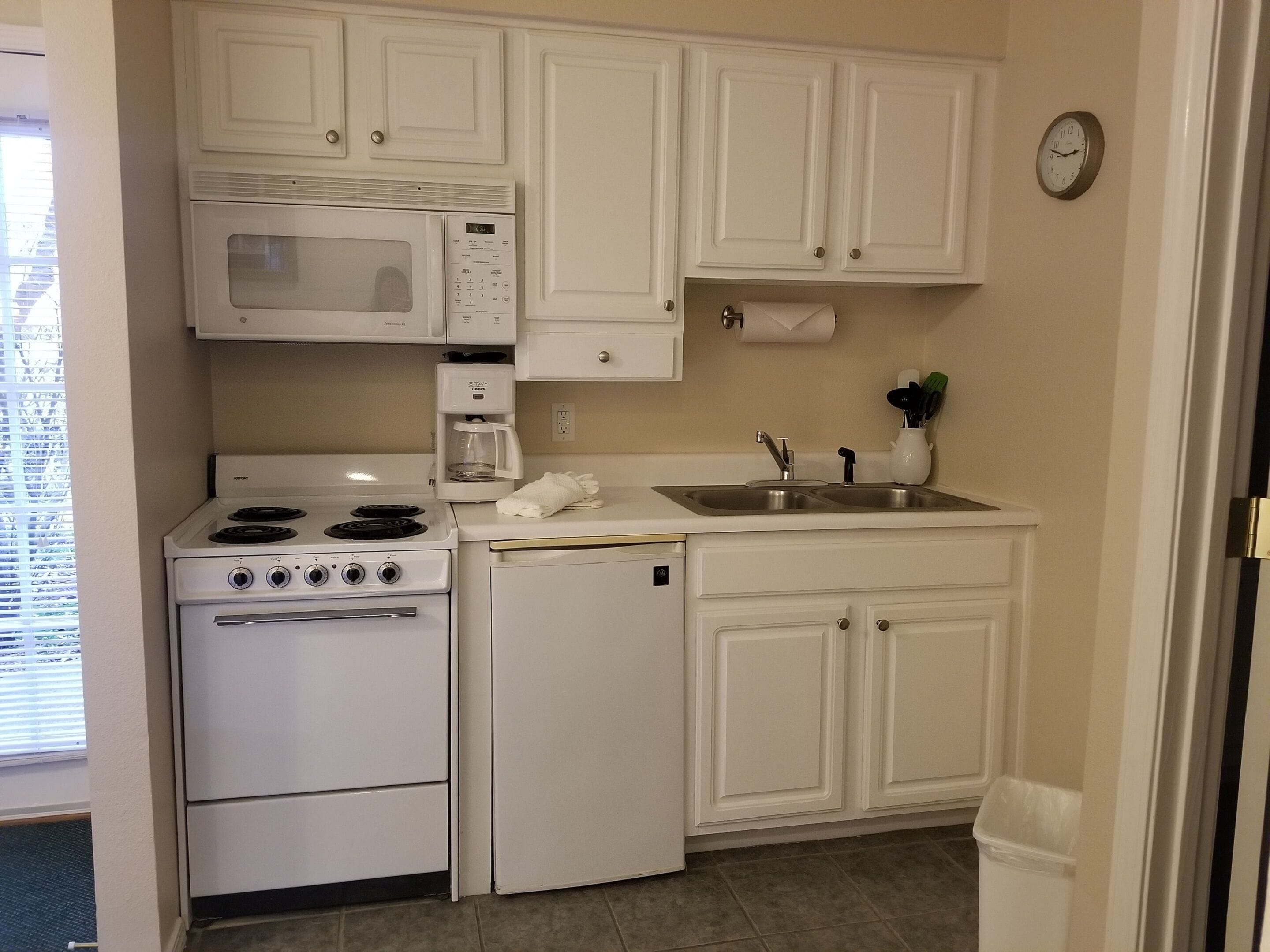 A compact kitchen with white cabinets, a microwave, a stove, a refrigerator, and a sink.