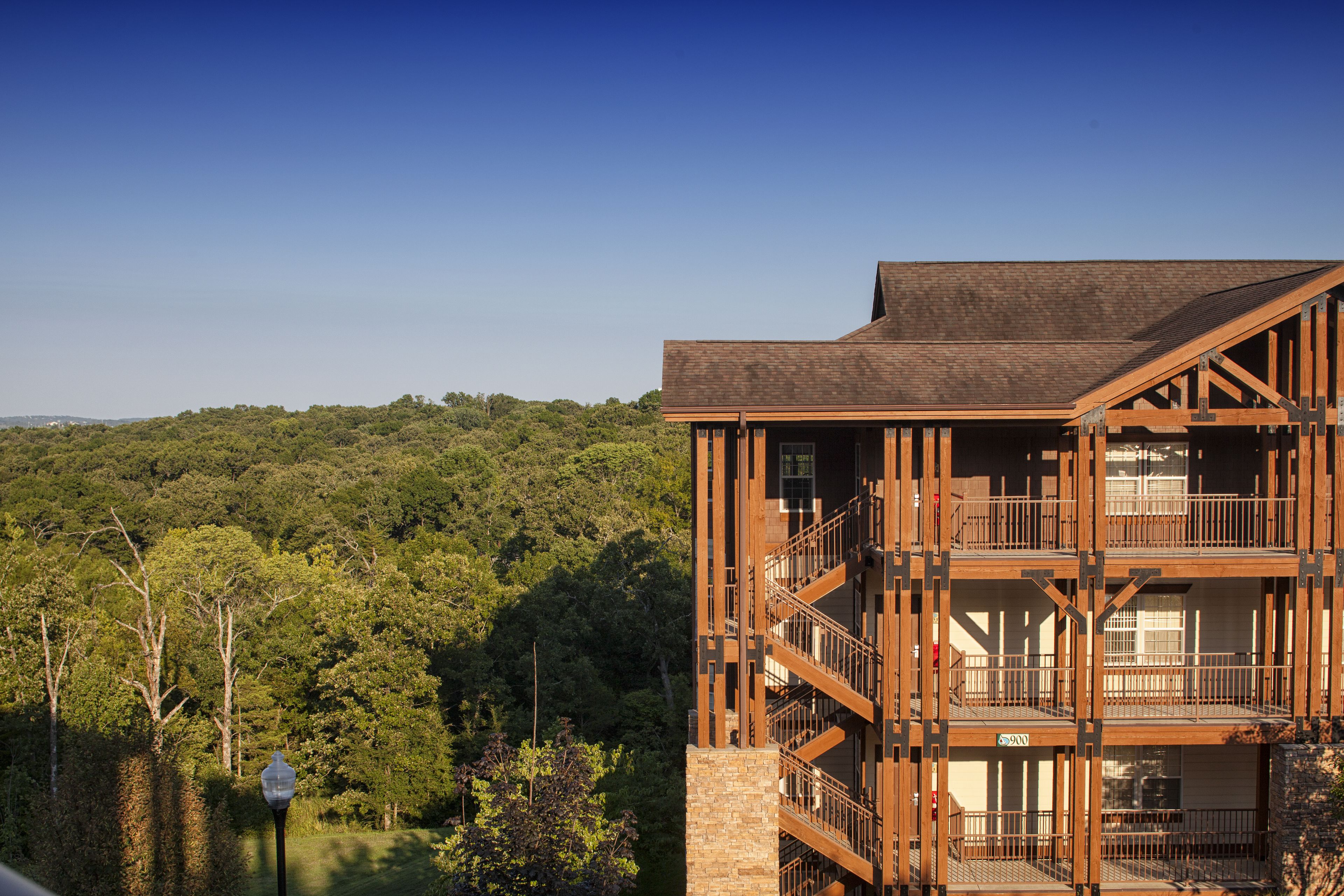 A multi-story building with a wooden exterior and multiple balconies, surrounded by a forested area.