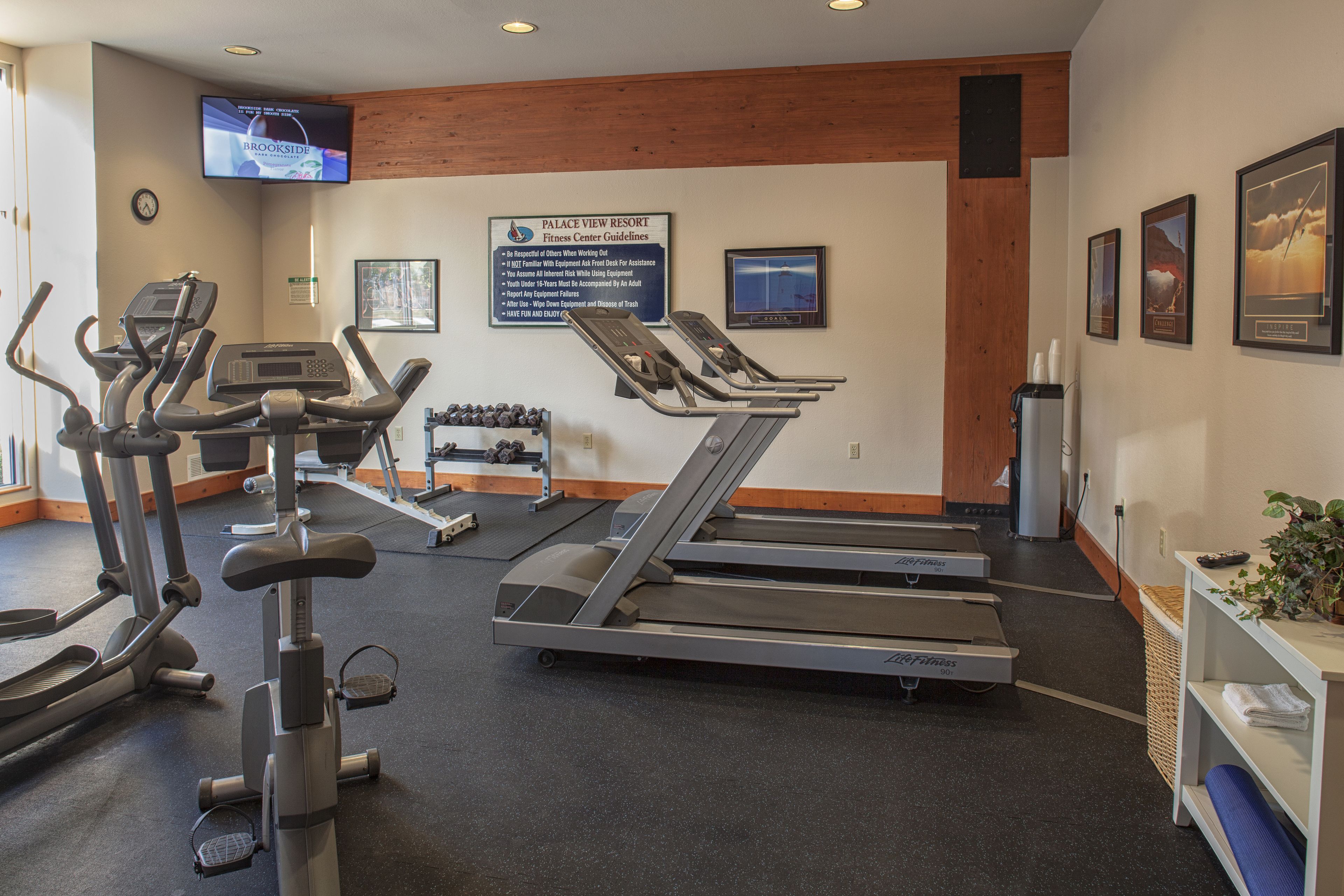 Un centre de remise en forme équipé de tapis de course, de vélos elliptiques et d’un téléviseur diffusant des programmes sur le fitness.