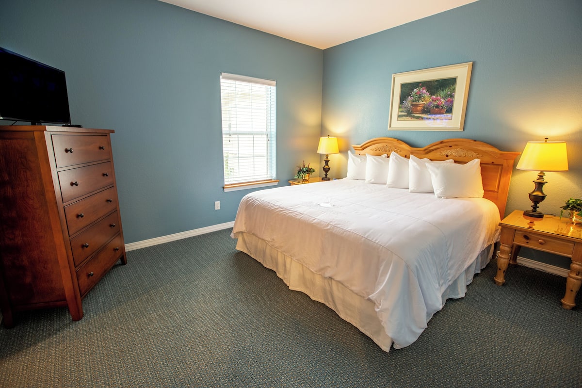 A bedroom with a bed, a dresser, a window, and two bedside lamps.
