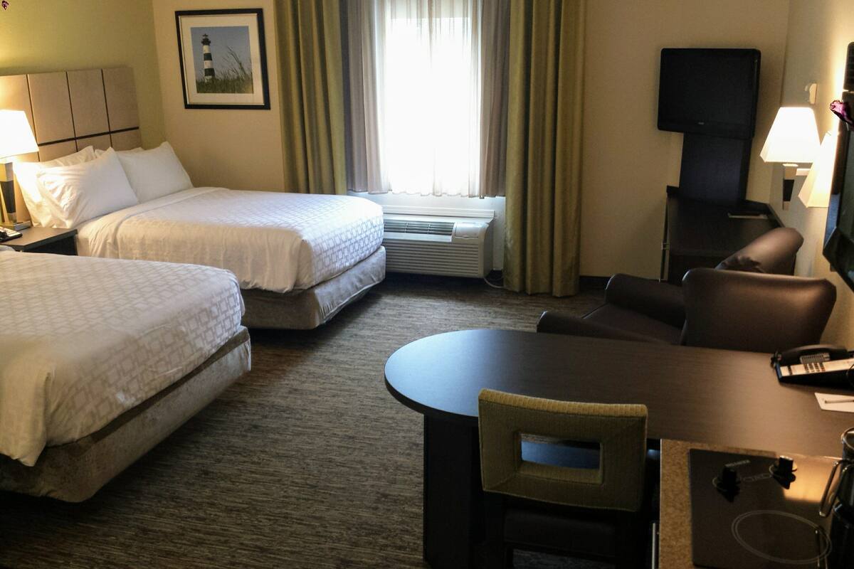 Une chambre d’hôtel avec deux lits, un canapé, une table, une télévision et une fenêtre avec des rideaux.