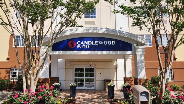 A hotel entrance with a sign reading 'Candlewood Suites.' There are potted plants and a mailbox in the foreground. - Candlewood Suites Greenville NC by IHG (Greenville)